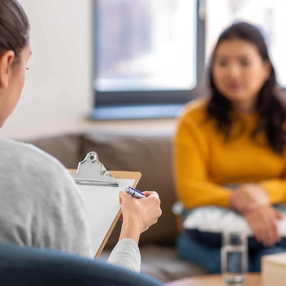 Selective focus image of a therapist holding a clipboard while talking to a client in therapy at QuickSilver Counseling Center