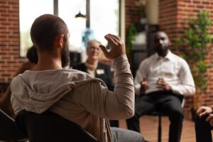 Person raising hand in group therapy while receiving addiction therapy services