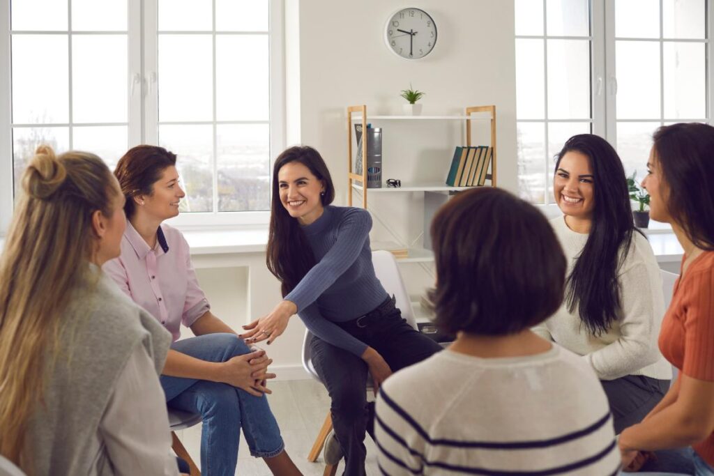 a woman supports another in a group as they discuss the benefits of Women's Rehab Program